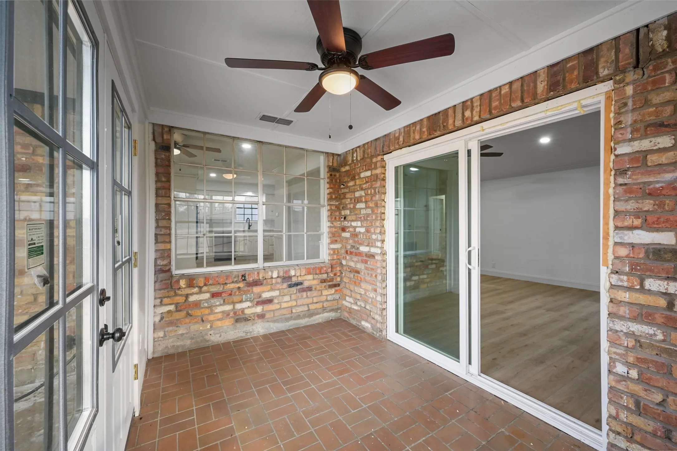 Covered patio featuring a ceiling fan, brick walls, and herringbone-patterned tile flooring