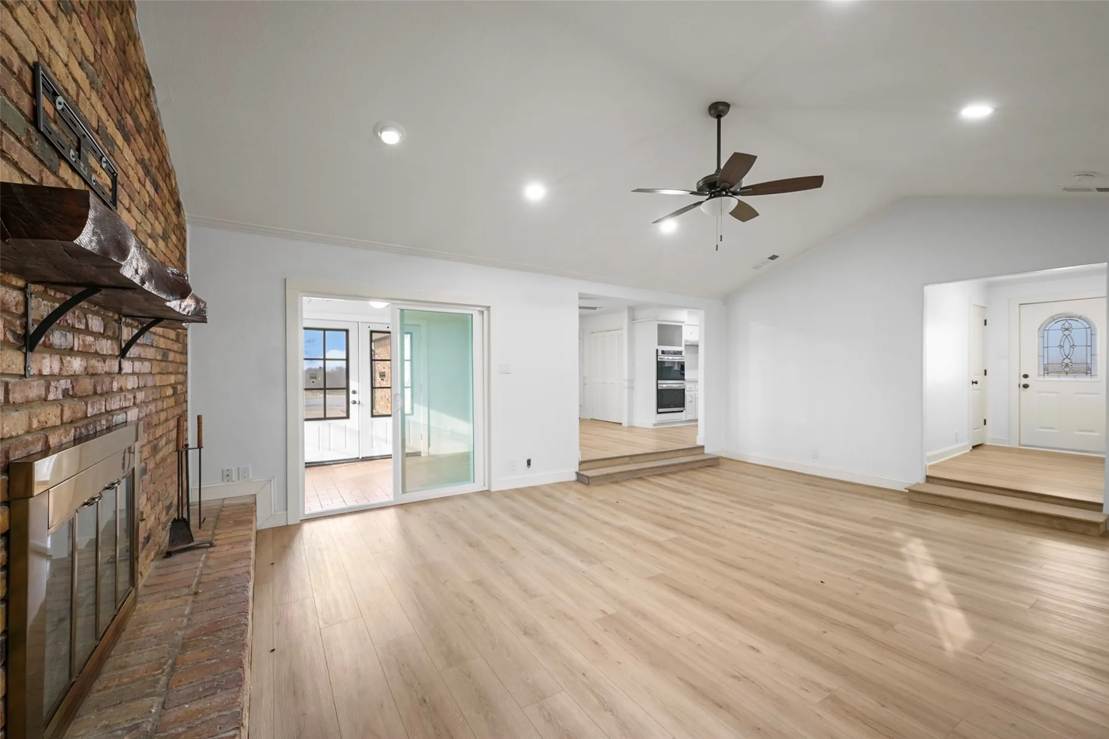 Exposed brick fireplace with a wood mantel, wood-finish flooring, vaulted ceiling, and recessed lighting