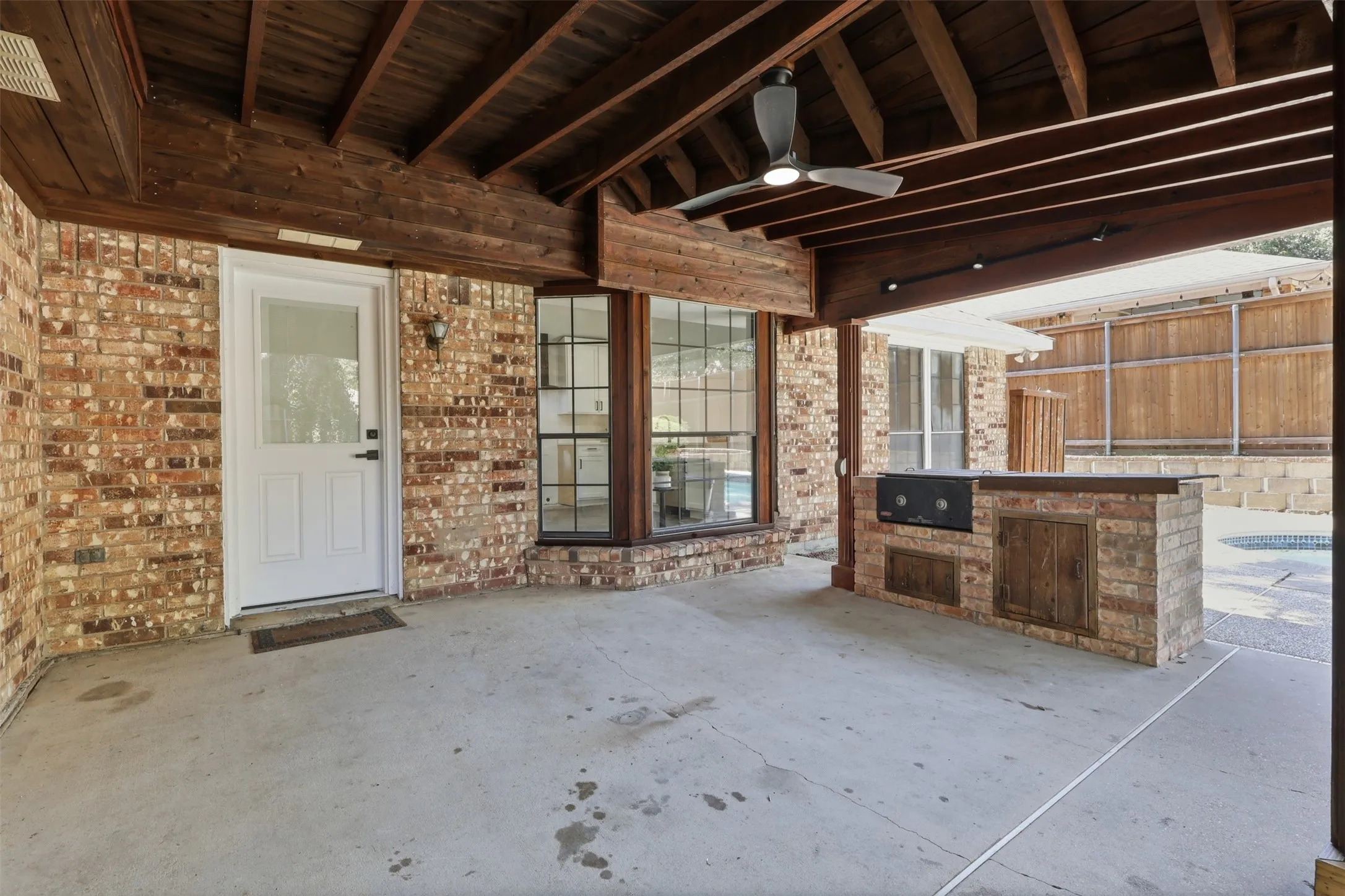 Covered outdoor living space featuring exposed wood beam ceiling, brick exterior walls, and a built-in brick grilling station with counter space