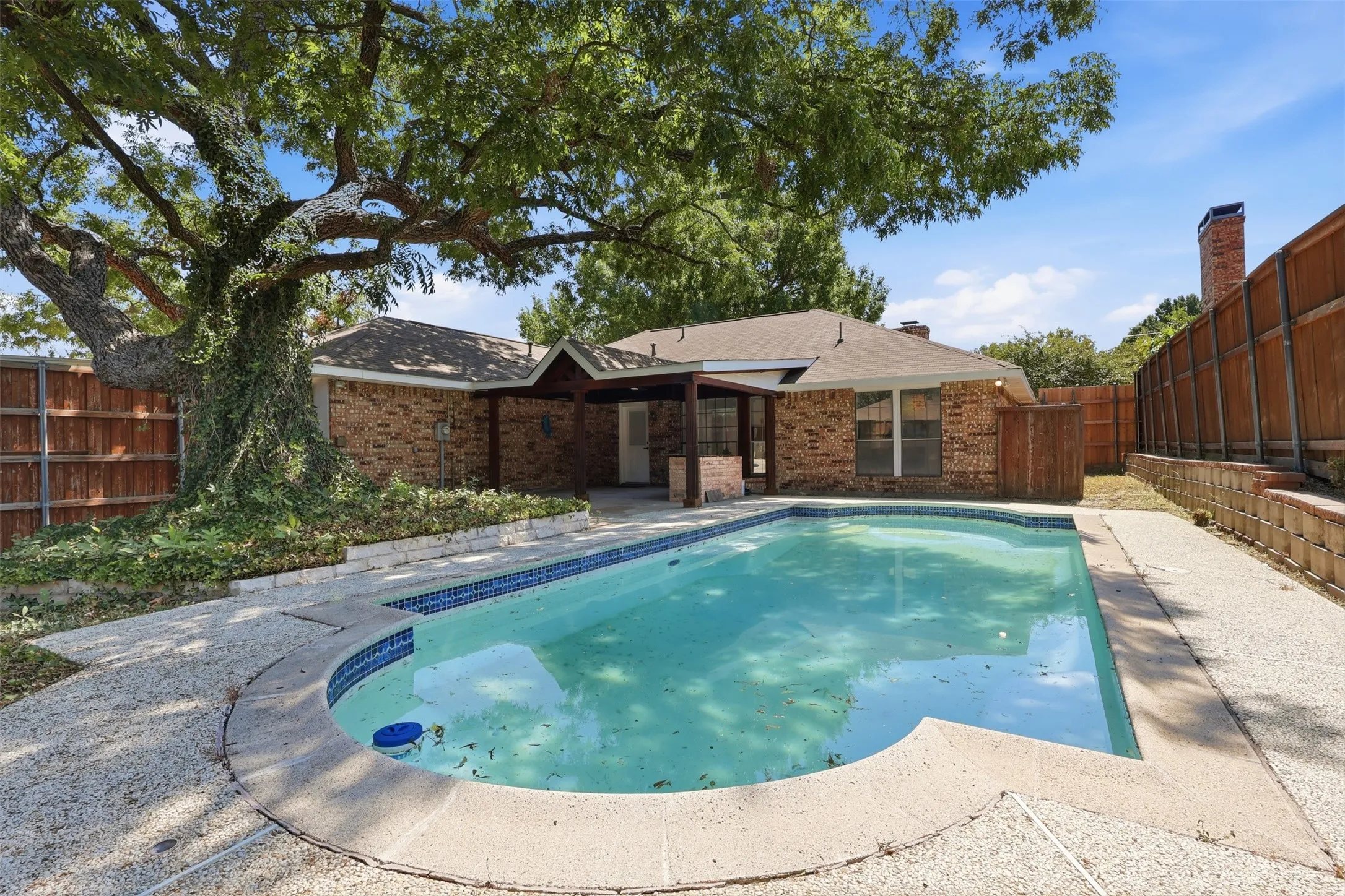 Brick exterior featuring a swimming pool, covered patio, mature tree, and wood fence