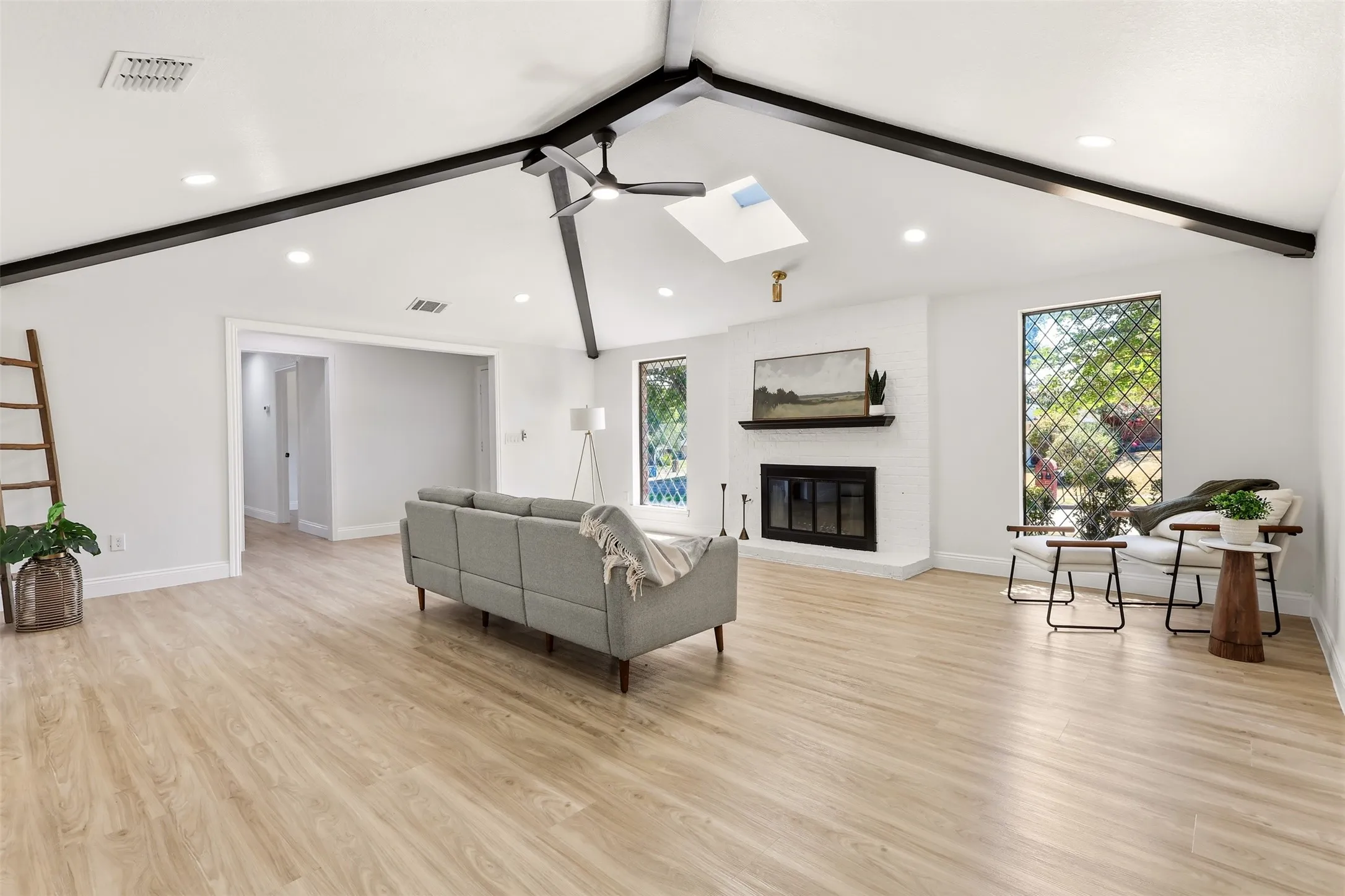 Spacious open-concept living area featuring vaulted ceilings with exposed black beams, recessed lighting, and large windows allowing natural light