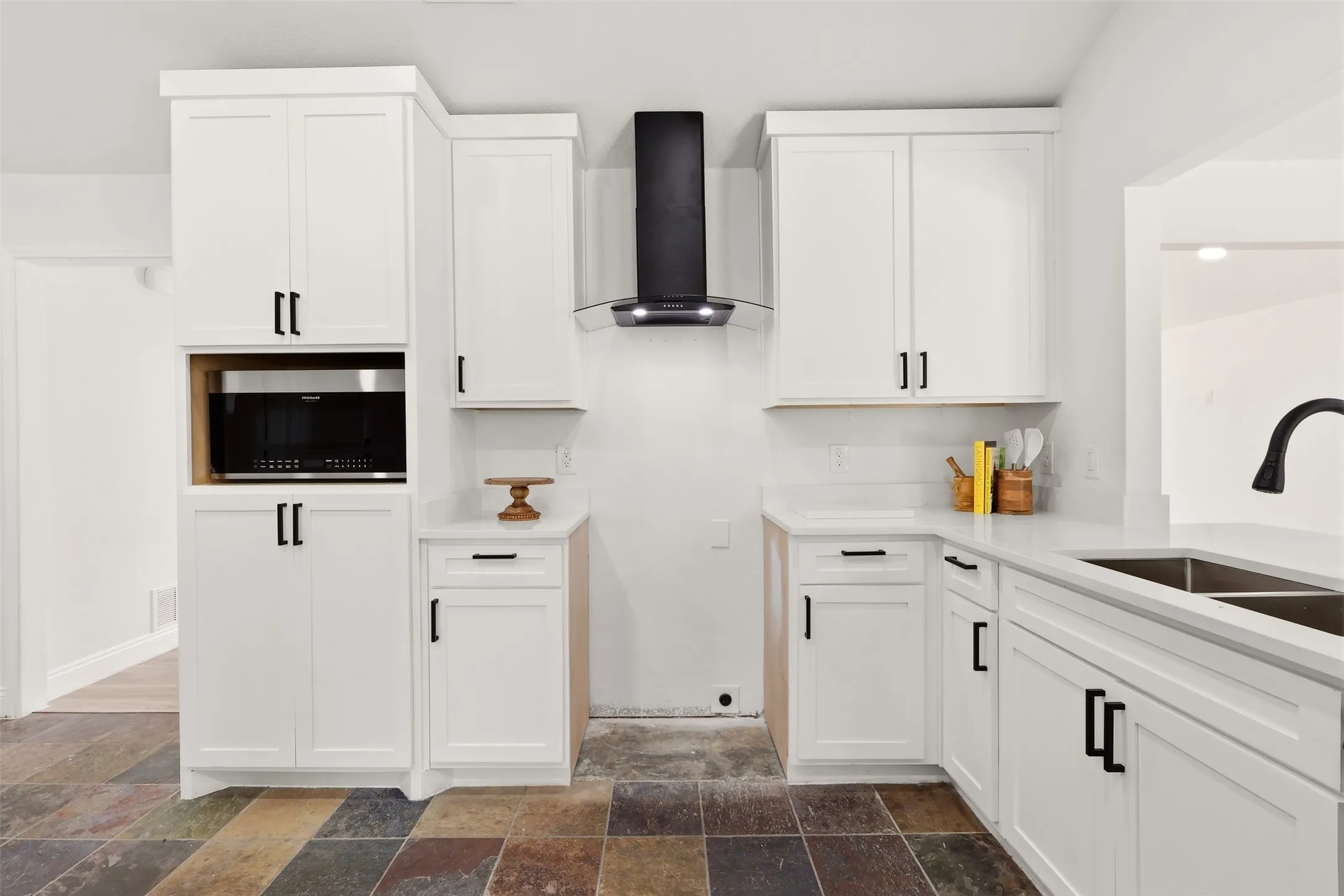 White shaker cabinetry with matte black hardware, built-in microwave, dark tile flooring, and a stainless steel double basin sink
