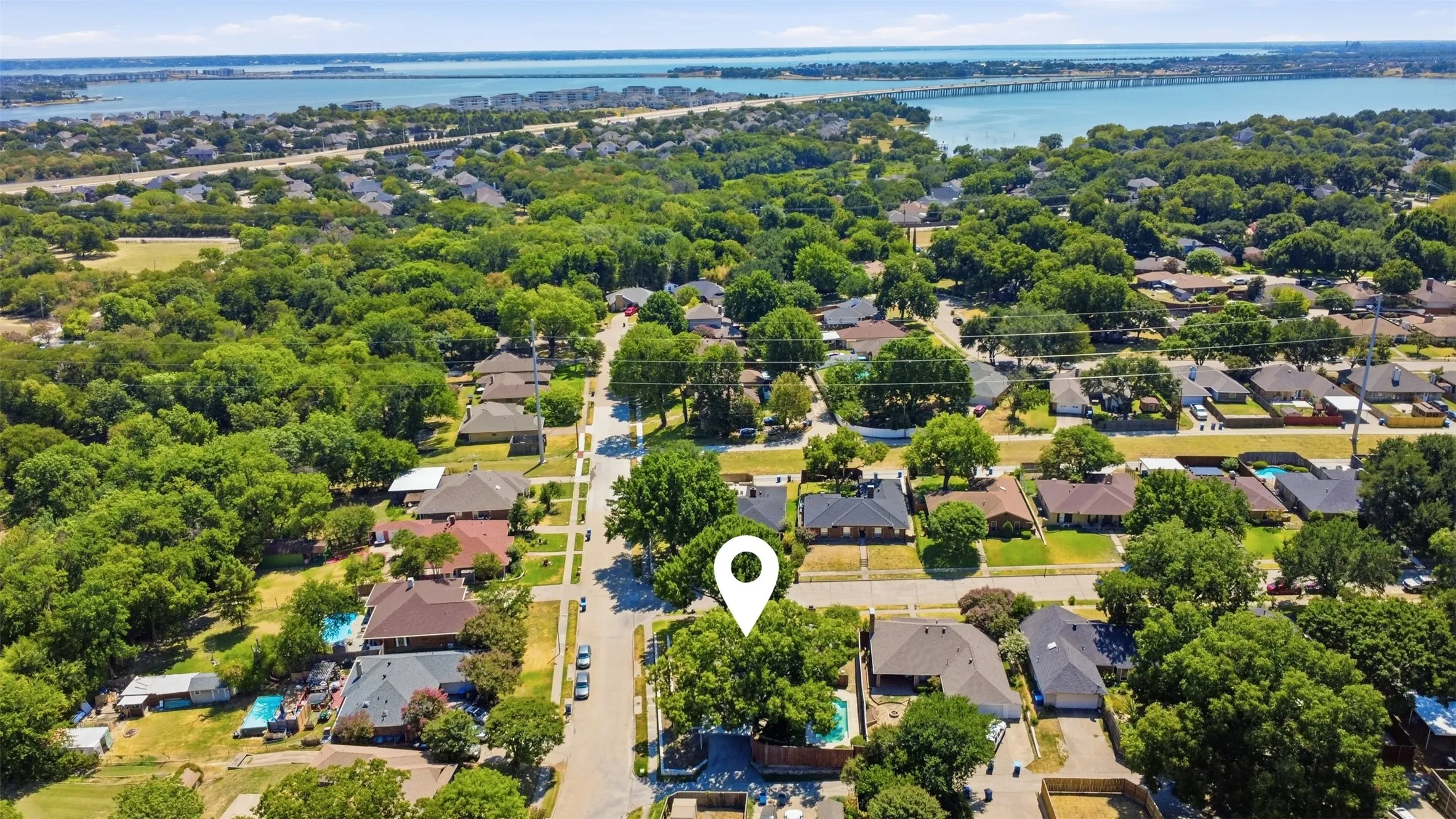 Aerial view showcasing a well-landscaped residential lot with mature trees, manicured lawn, and established neighborhood setting near waterfront areas
