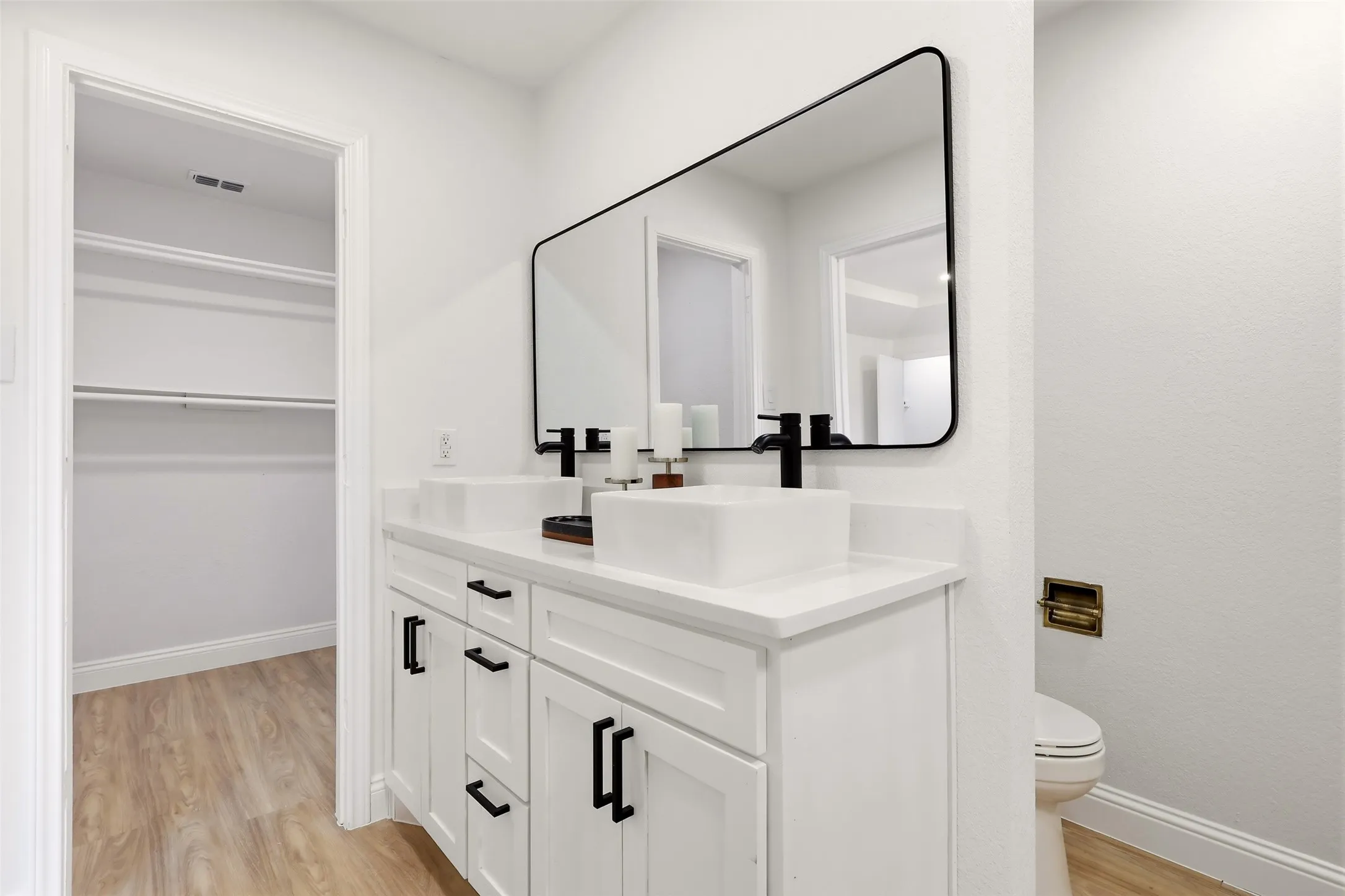 Modern primary bathroom featuring a white vanity with dual black hardware pulls, white quartz countertop, white vessel sink, and matte black faucet