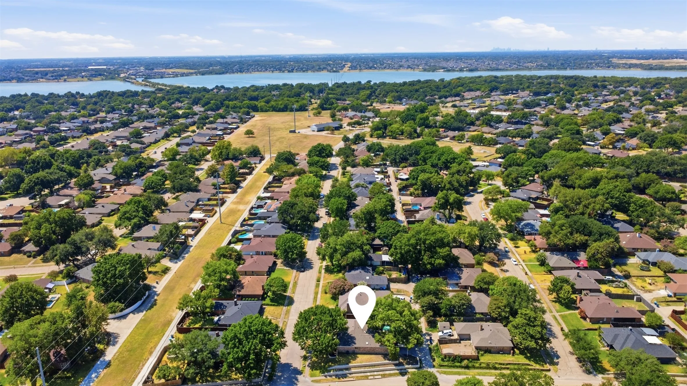 Expansive neighborhood featuring mature trees and established residences, with a prominent lake and bridge visible in the distance