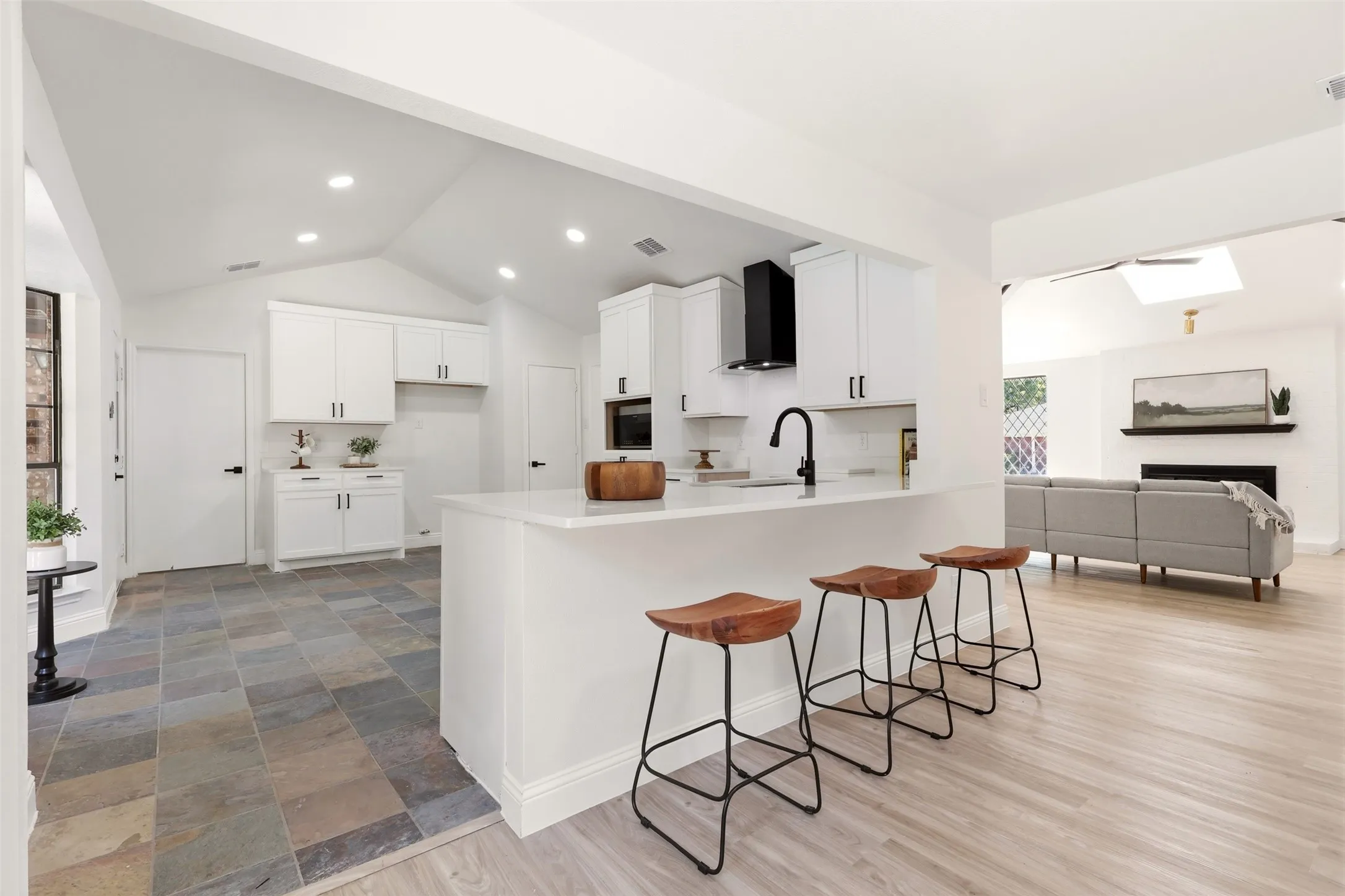Kitchen island with a bright countertop, white cabinetry with black hardware, black range hood, and a black faucet