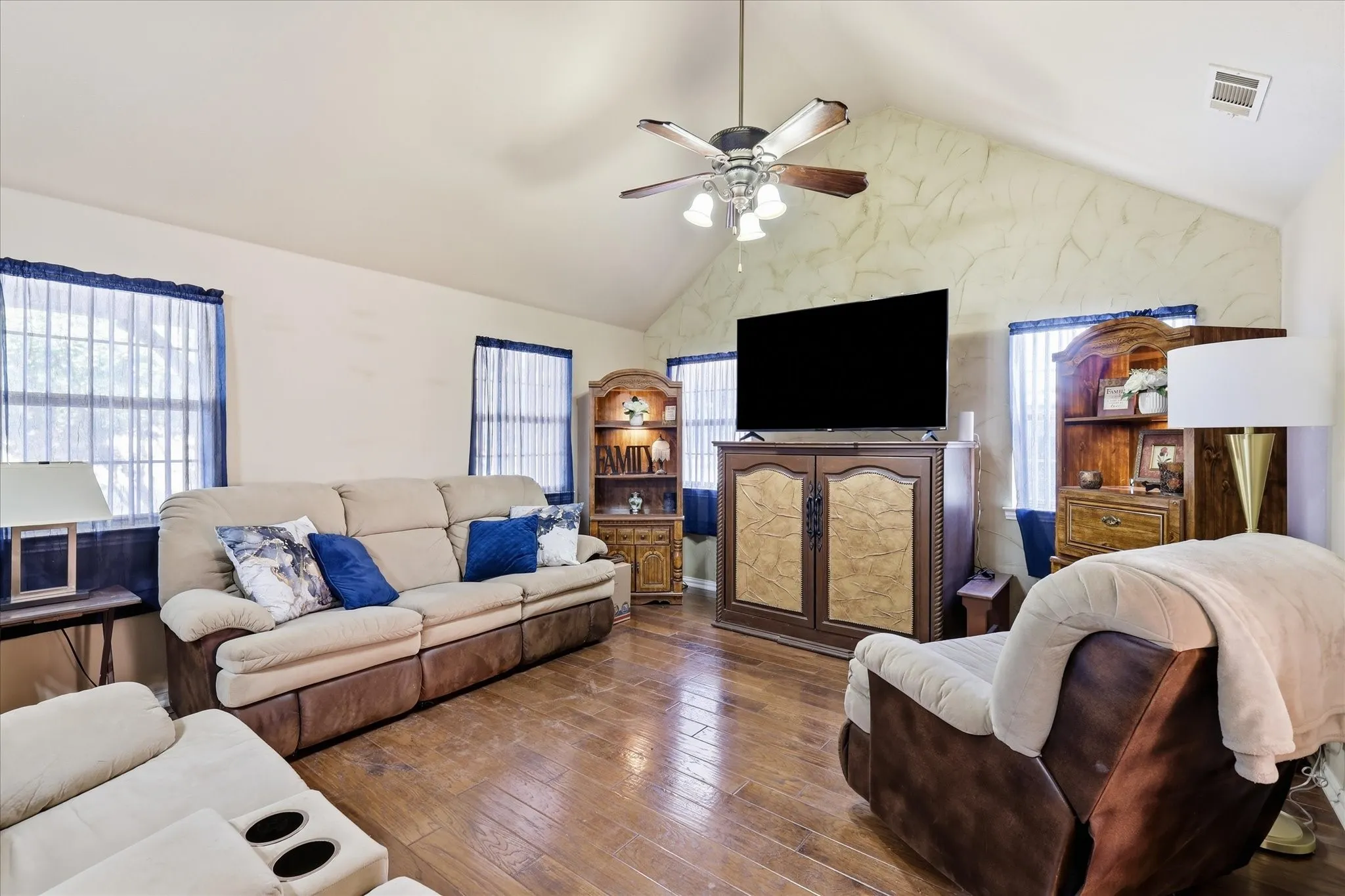 Vaulted ceiling with a ceiling fan, wood-finish flooring, and multiple windows