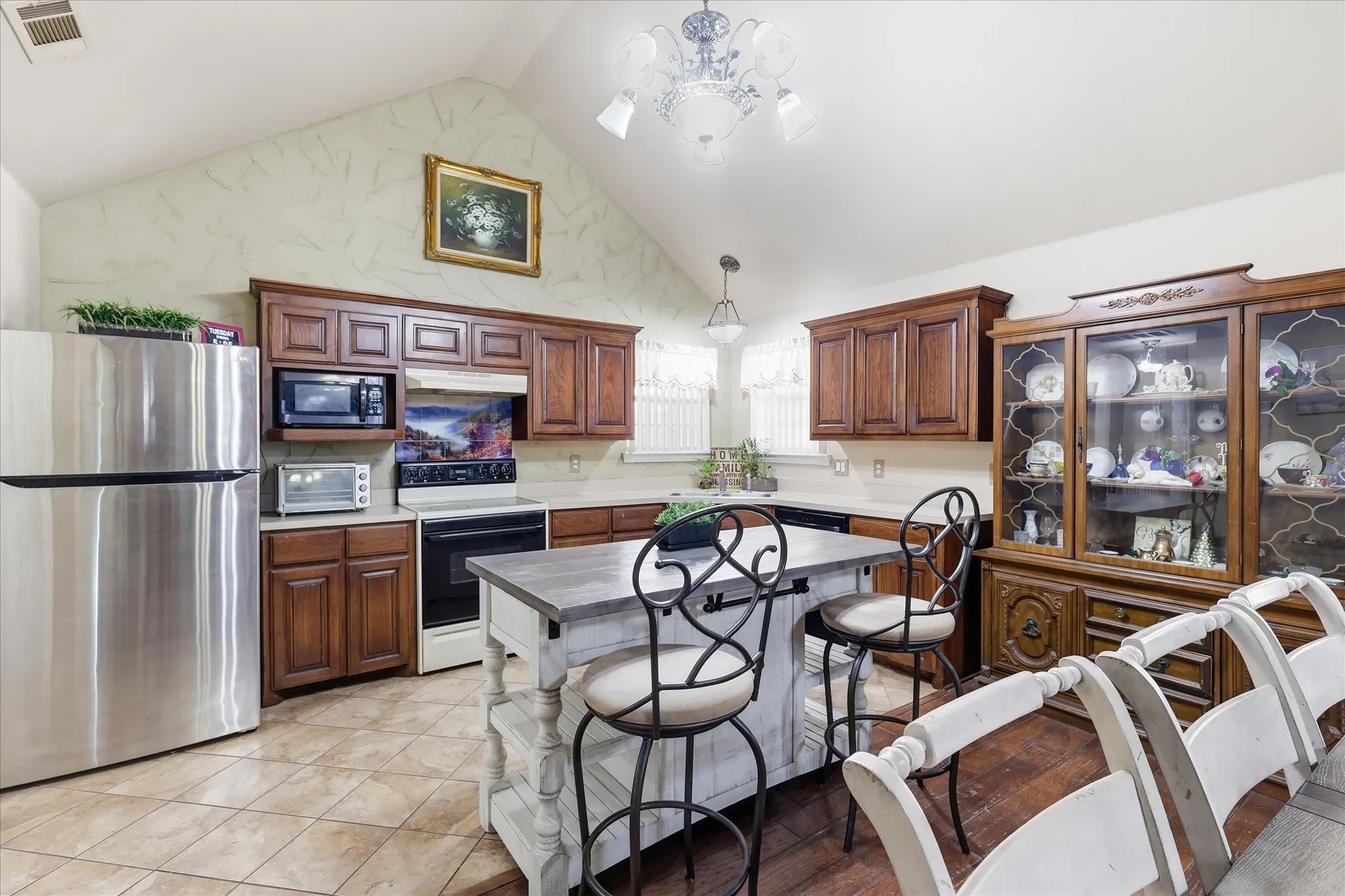 Vaulted ceiling with a decorative chandelier, recessed lighting, tile flooring, and wood-finish cabinetry
