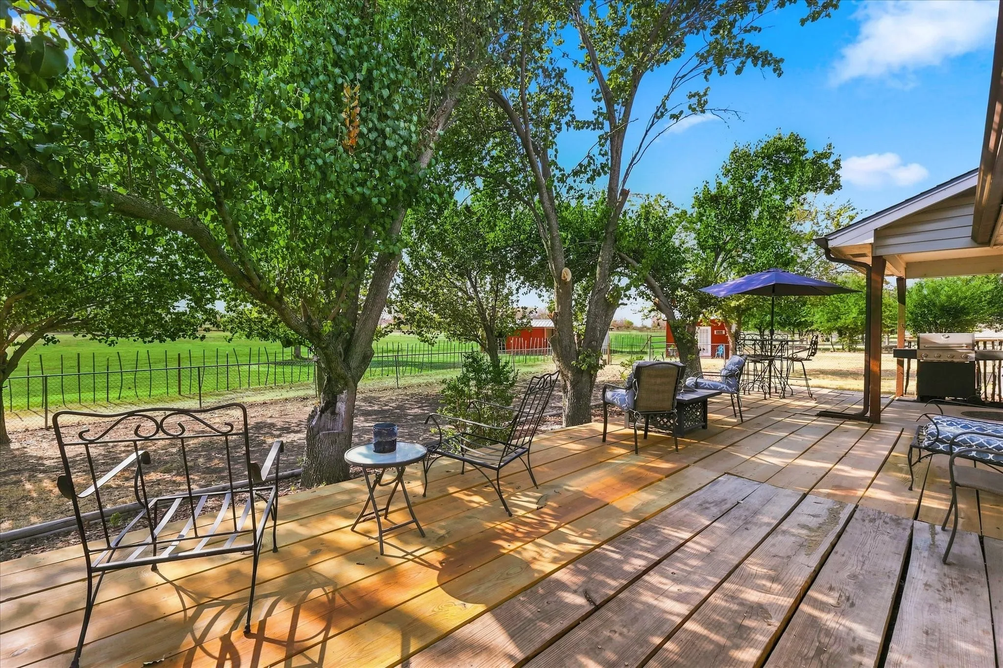 Expansive wood deck with mature trees, covered patio, and outdoor grilling area