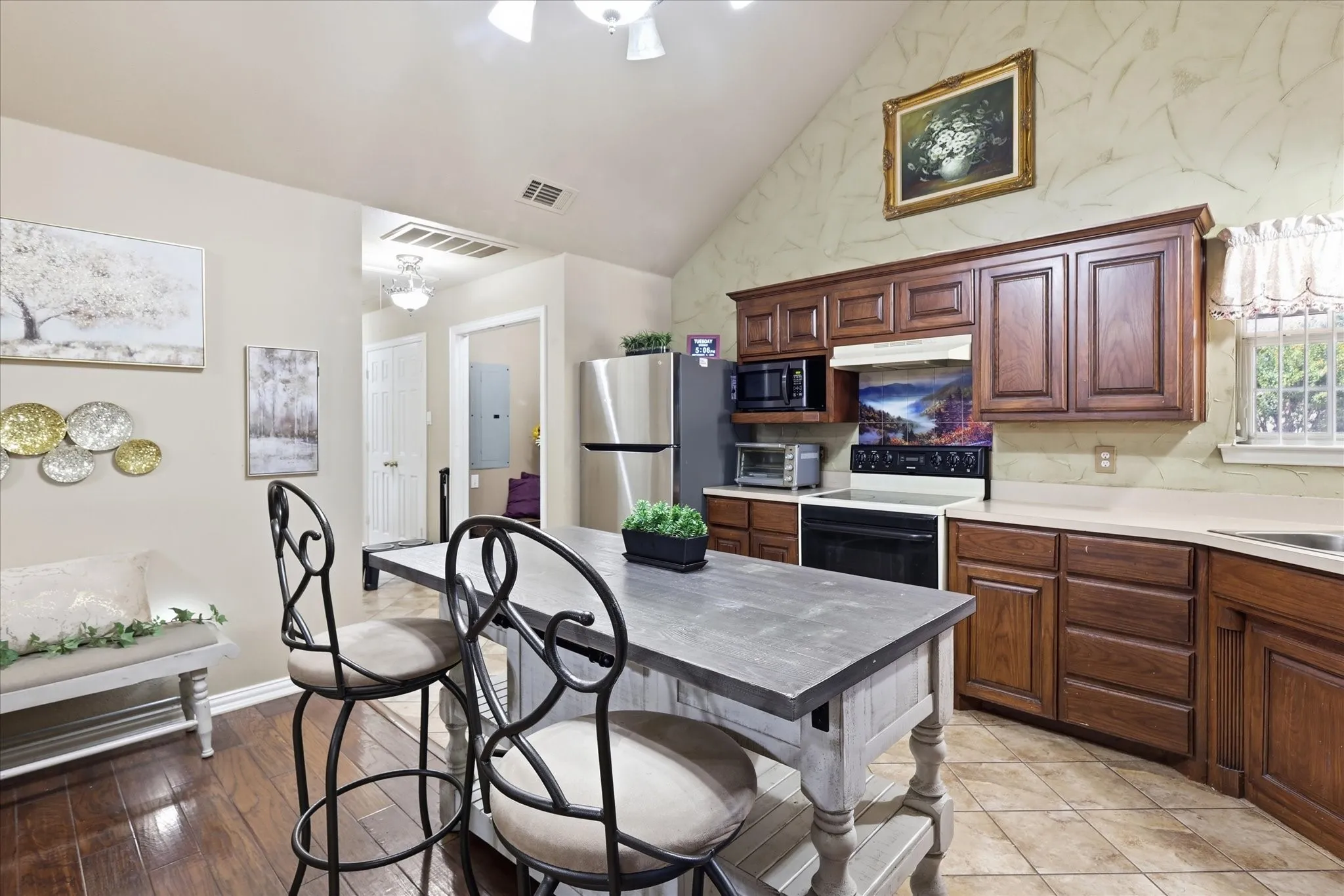 Kitchen with vaulted ceiling, wood-finish cabinetry, tile flooring, and a stainless steel refrigerator
