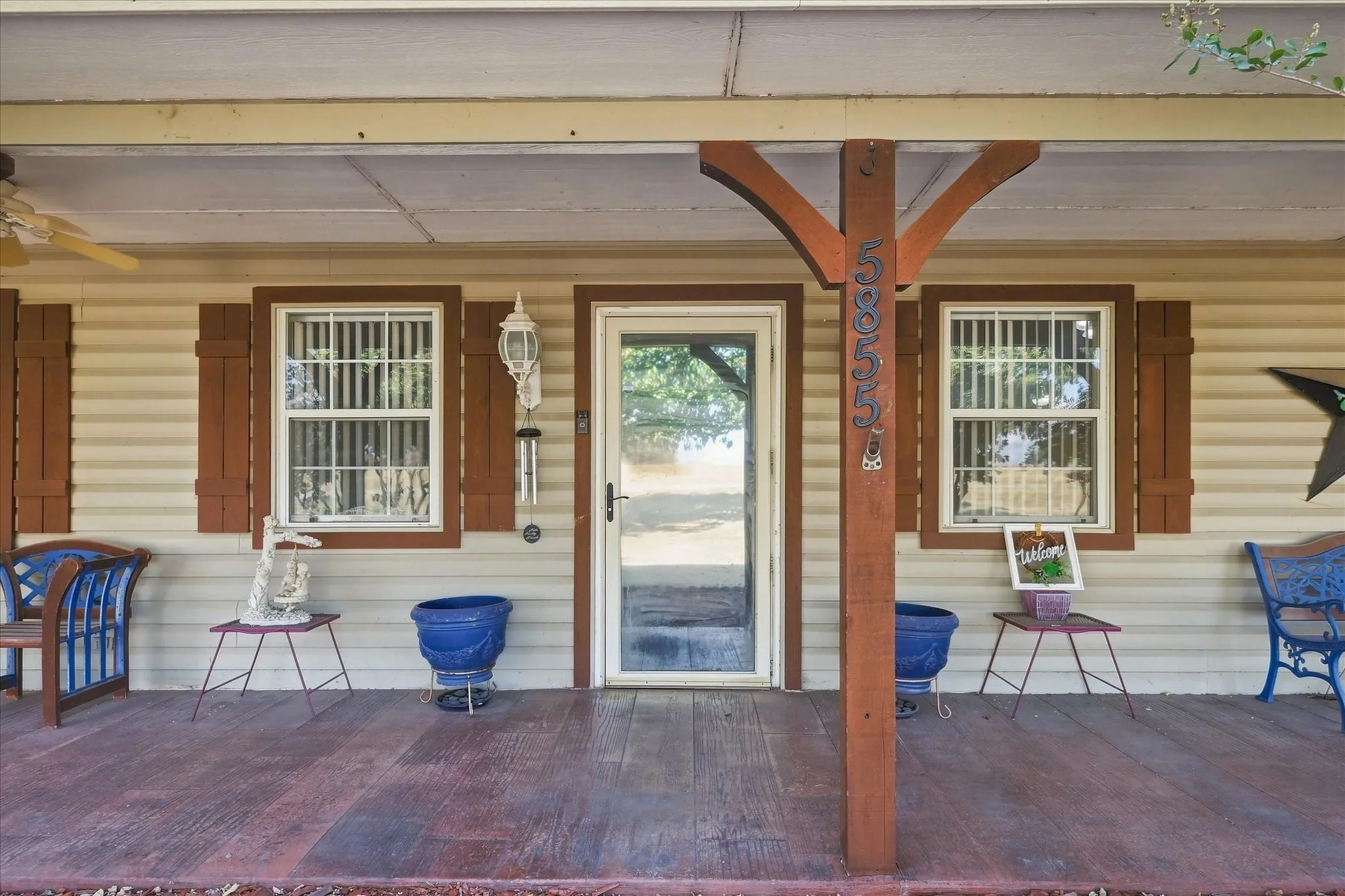Front porch with wood-finish flooring, two windows with brown shutters, and a central entry door with a screen