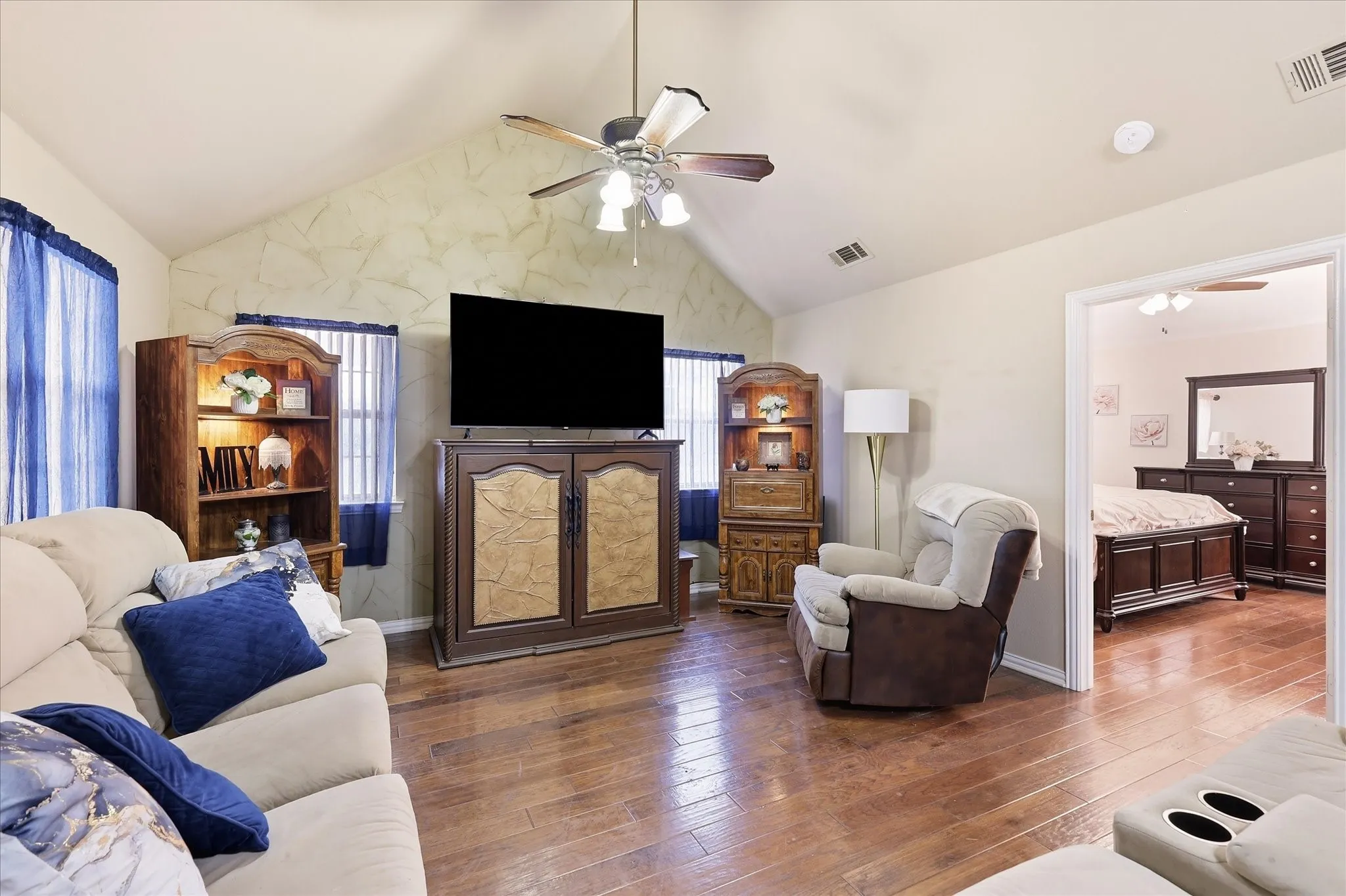 Vaulted ceiling with a ceiling fan, wood-finish flooring, and a doorway opening to another room