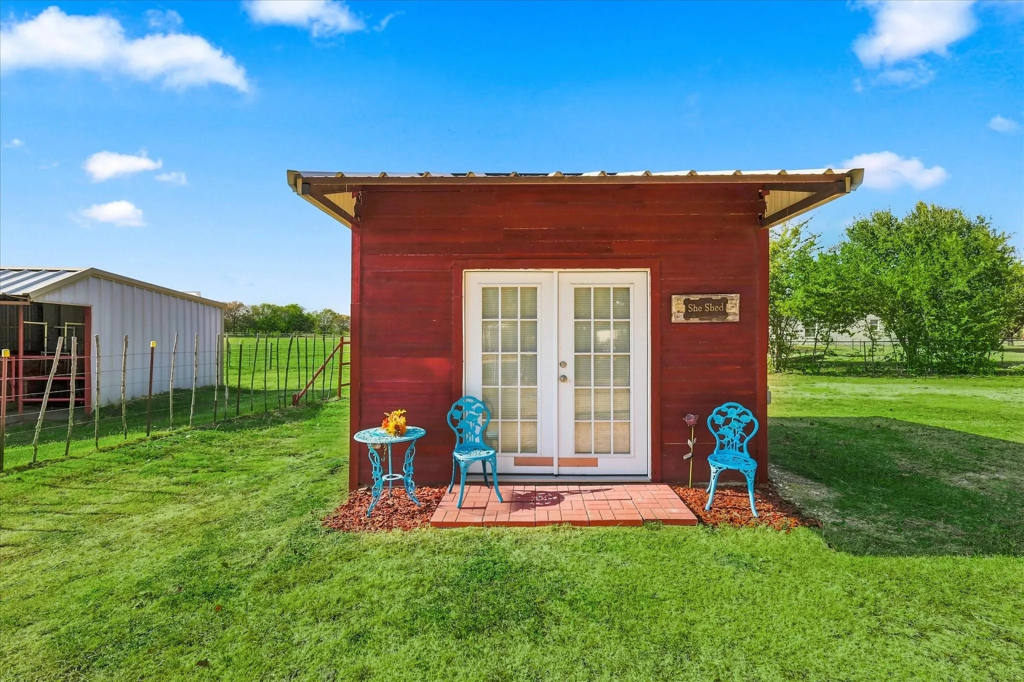 Red-sided auxiliary structure with a pitched roof, double glass-paneled entry doors, and a brick-paved patio area