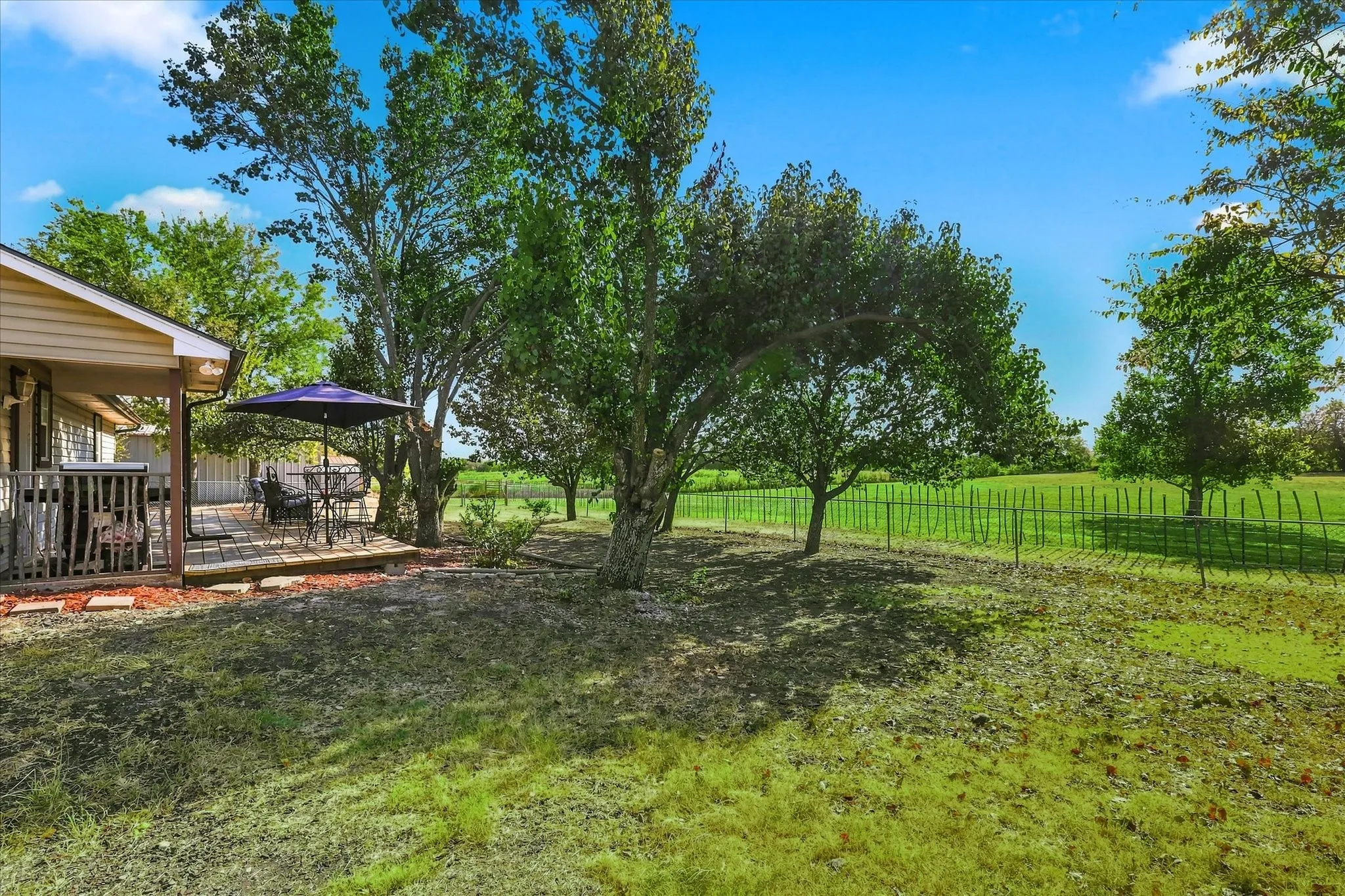 Expansive exterior space with a raised wooden deck, mature trees, and a green landscape