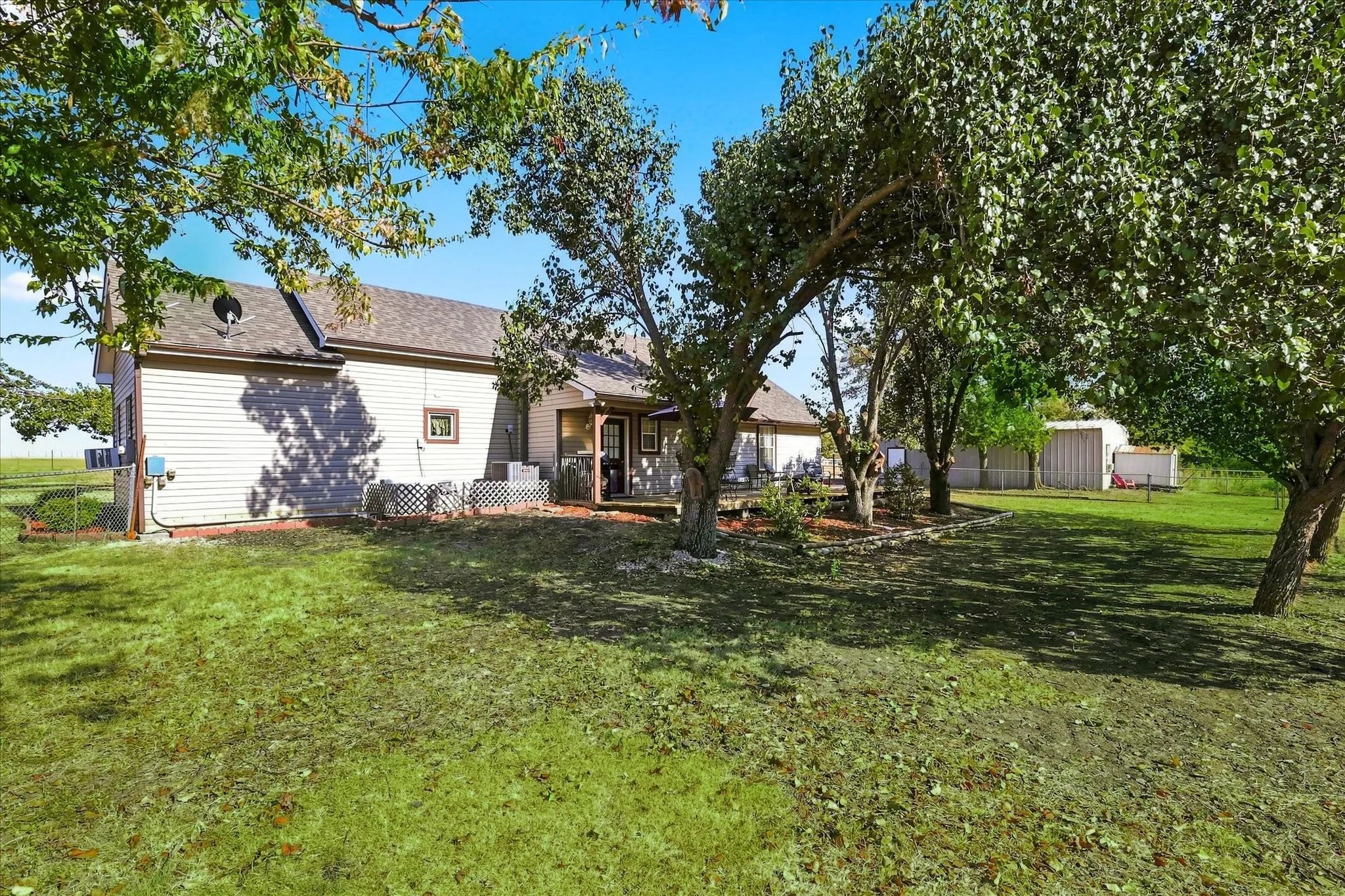 Exterior siding, covered porch, mature trees, partial fencing, and a detached structure