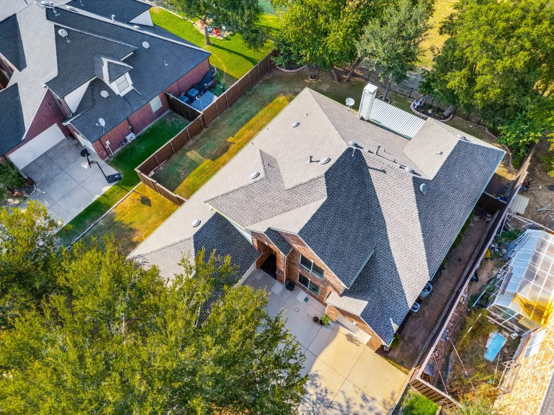 Expansive shingle roof, brick exterior, concrete driveway, and surrounding mature trees