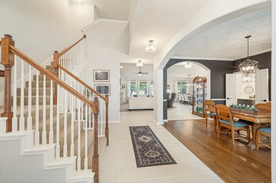 Grand staircase with wood handrails and carpeted treads, complemented by arched doorways, tile flooring, and wood-finish flooring in the dining area