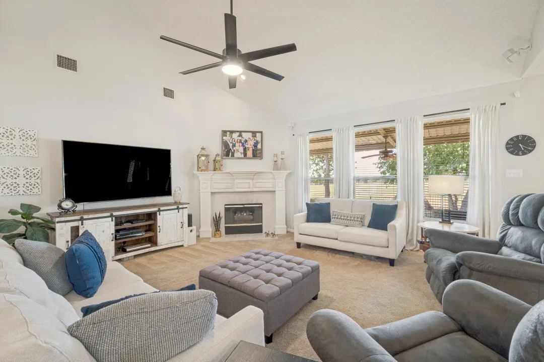 Vaulted ceiling with a ceiling fan, fireplace with a mantel, multiple windows, and carpet flooring