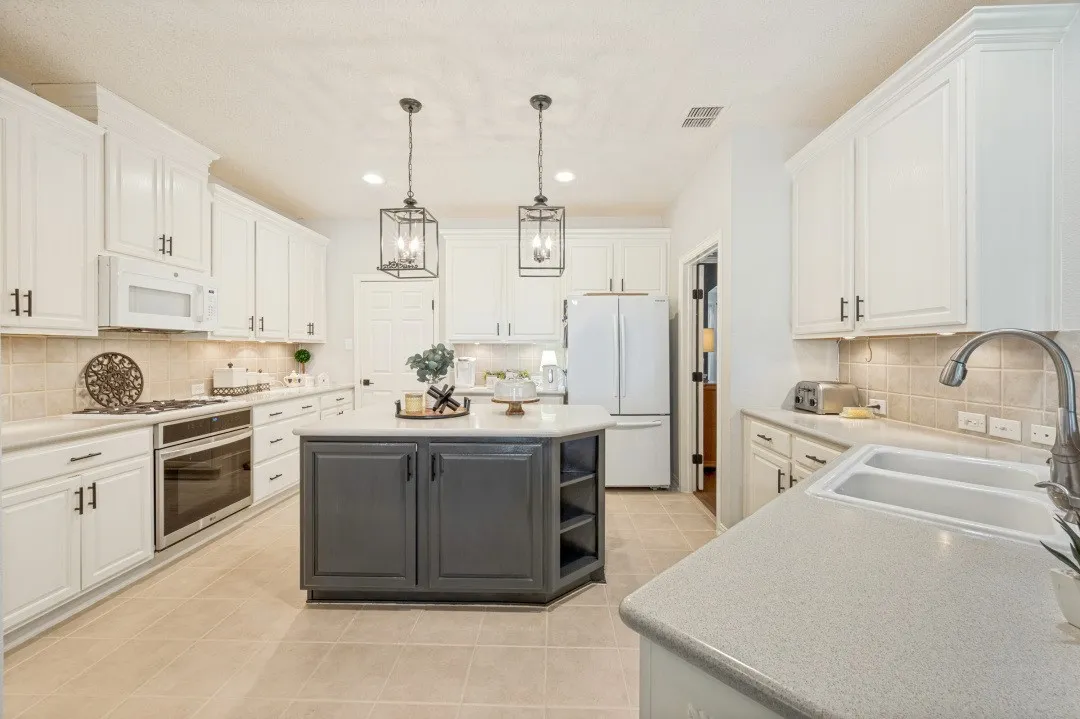 White cabinetry with dark hardware, a center island featuring open shelving, light-toned tile flooring, recessed lighting, and stainless steel appliances