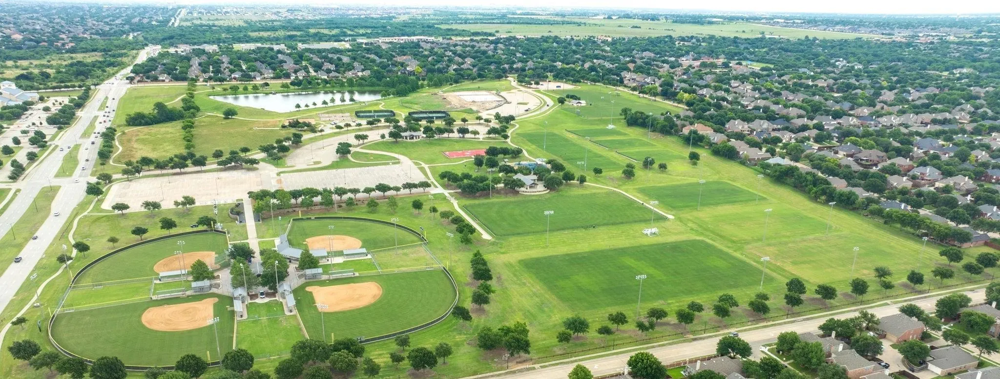 Expansive recreational grounds featuring multiple baseball fields, soccer fields, and a pond