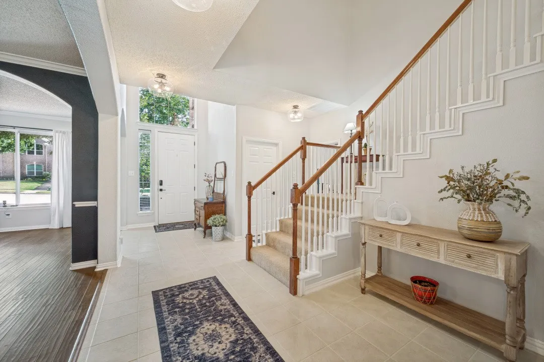Two-story foyer with tile flooring, wood-finish staircase with white balusters, and transom window above the entry door