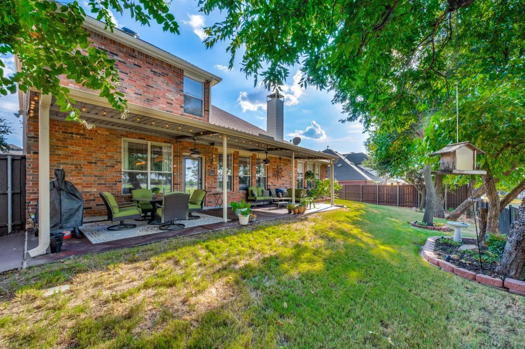 Expansive backyard featuring a brick exterior, covered patio, and mature trees