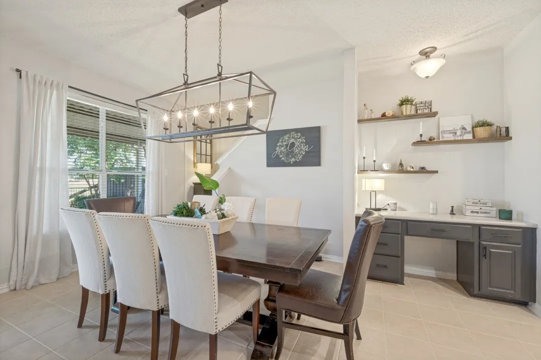 Expansive dining area featuring a rectangular chandelier, a window with blinds, tile flooring, and a built-in desk with shelving