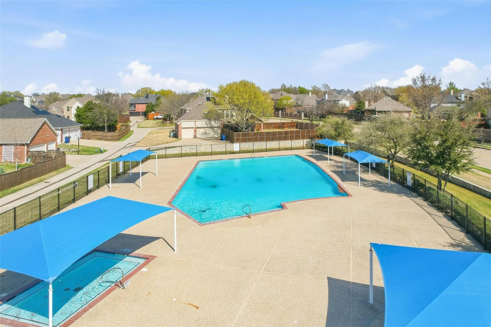 Community swimming pool with surrounding concrete decking, multiple shade structures, and adjacent smaller pool