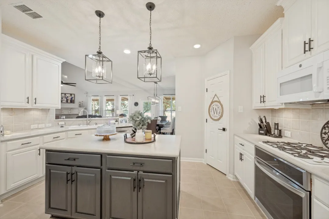 Kitchen featuring a central island, white cabinetry, integrated stainless steel appliances, and two pendant light fixtures