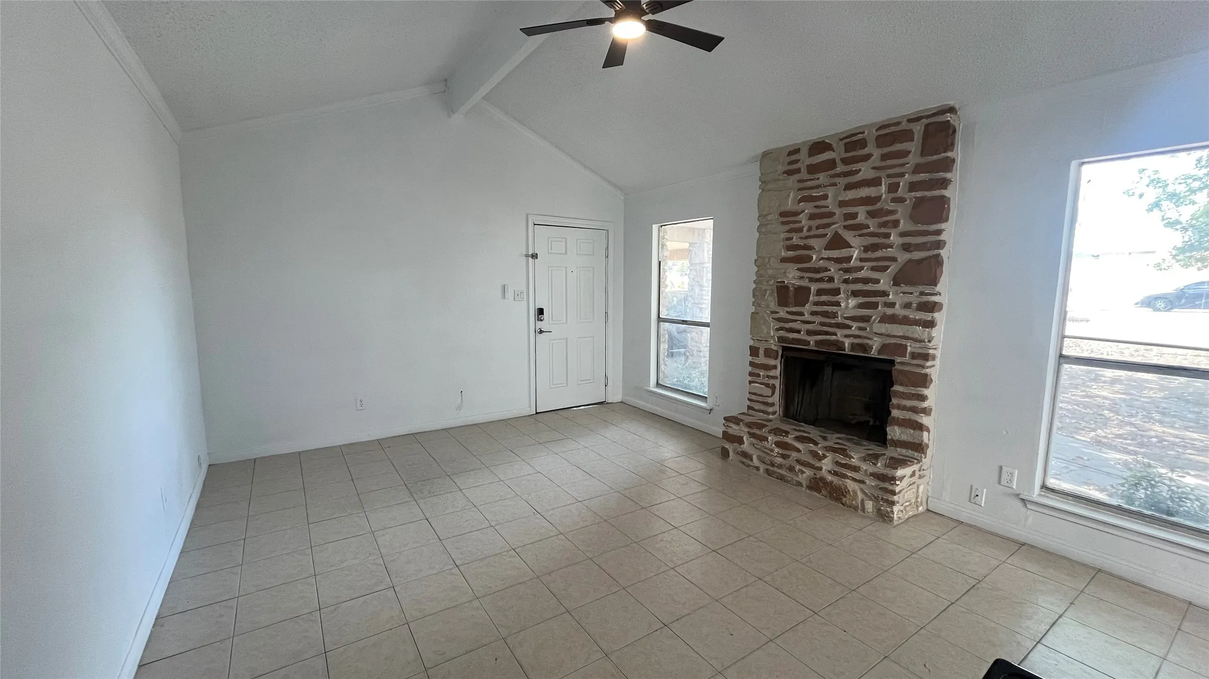 Vaulted ceiling with a ceiling fan, stone-clad fireplace, tiled flooring, and multiple windows