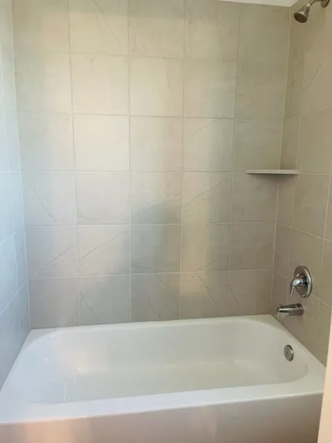 Full-size bathtub with a tile surround and a built-in shower shelf