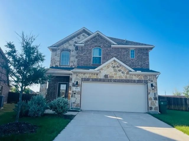 Two-story exterior with a brick and stone facade, arched windows, attached garage, and paved driveway