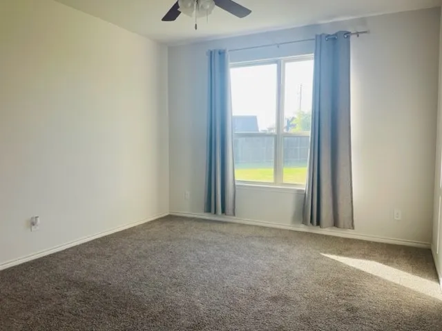 Carpeted room featuring a ceiling fan, a window with a white frame, and light-toned walls