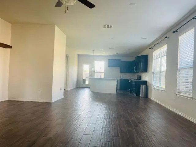 Wood-finish flooring throughout, ceiling fan, recessed lighting, kitchen with dark cabinetry, kitchen island with breakfast bar