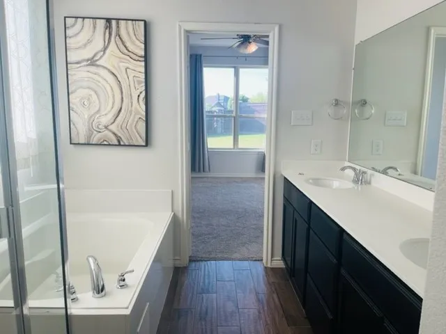 Bathroom featuring a built-in tub, dual vanity with undermount sinks, wood-finish flooring, and a large mirror