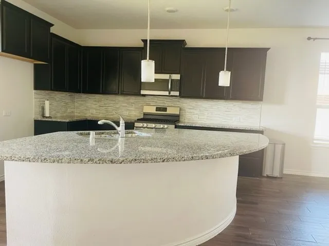 Kitchen featuring an island with stone countertop, stainless steel appliances, dark wood-finish cabinetry, a tile backsplash, and wood-finish flooring