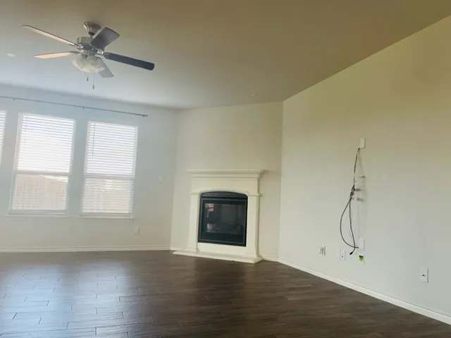 Wood-finish flooring, ceiling fan, multiple windows with blinds, and a built-in fireplace with a white mantel
