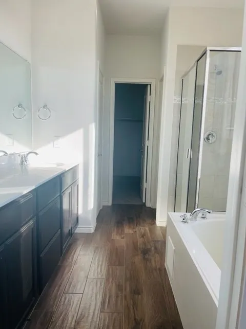 Double vanity with dark wood-finish cabinetry, built-in soaking tub, glass-enclosed shower, and wood-finish flooring