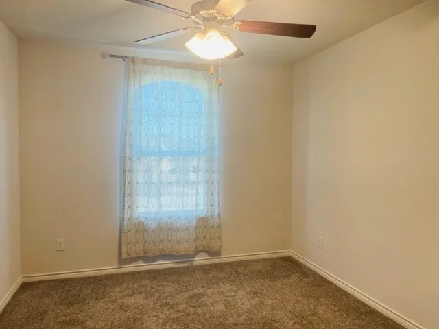 Neutral wall paint, ceiling fan with integrated lighting, window with arched detail, and plush carpet flooring