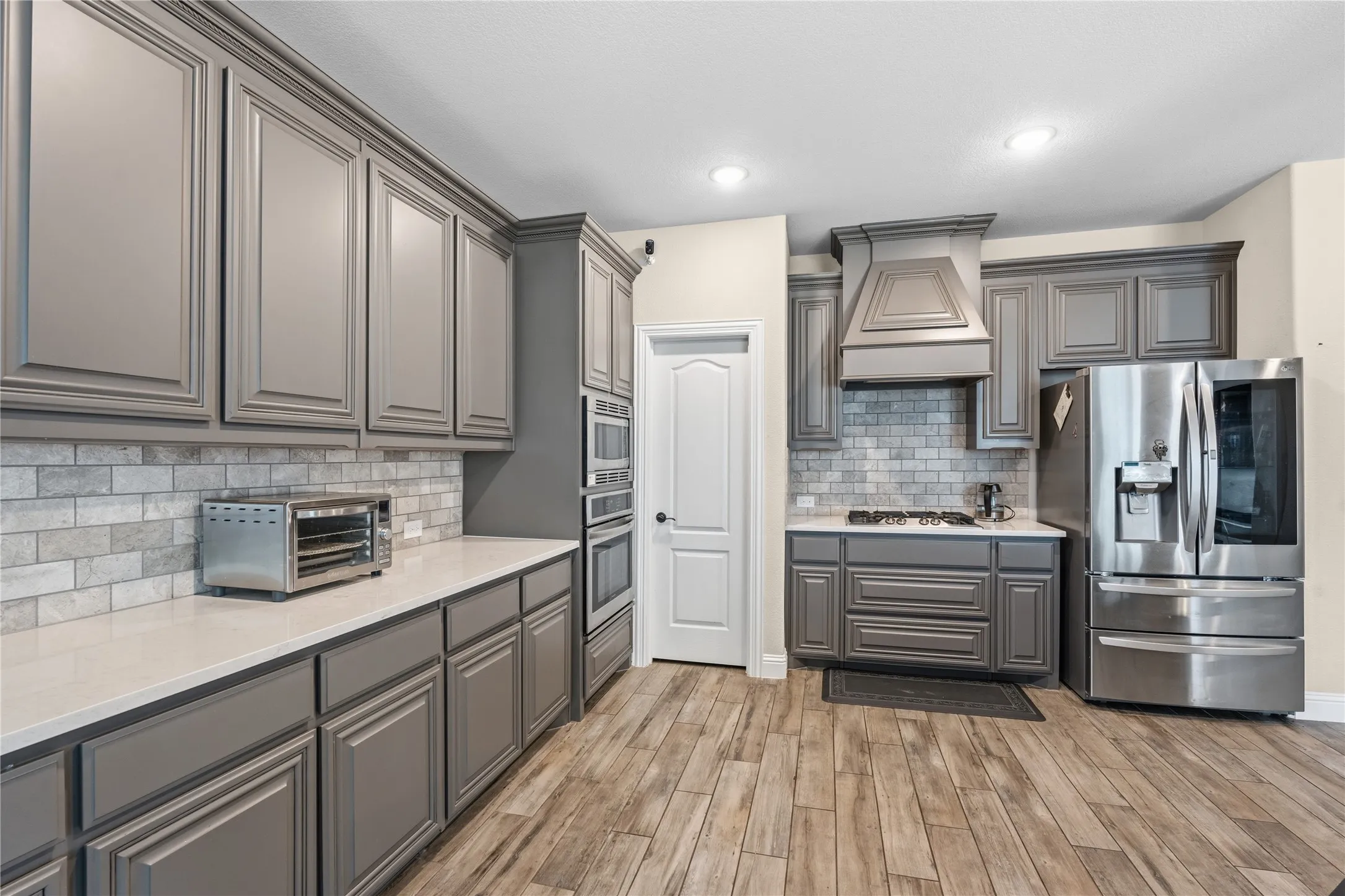 Kitchen featuring gray cabinetry, stainless steel appliances, light wood finished floors, light stone countertops, and recessed lighting