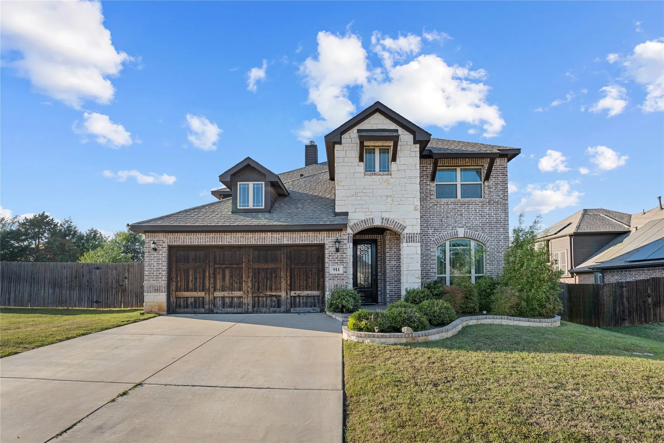 French country inspired facade with brick siding, an attached garage, concrete driveway, and stone siding