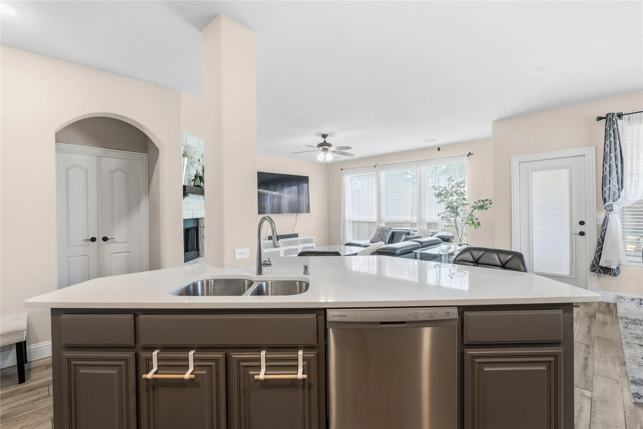 Kitchen featuring dishwasher, open floor plan, light wood-style flooring, a ceiling fan, and an island with sink