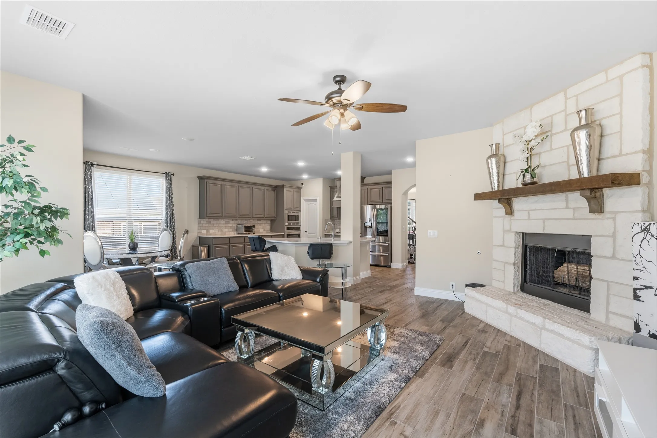 Living room with ceiling fan, dark wood-type flooring, a stone fireplace, recessed lighting, and arched walkways