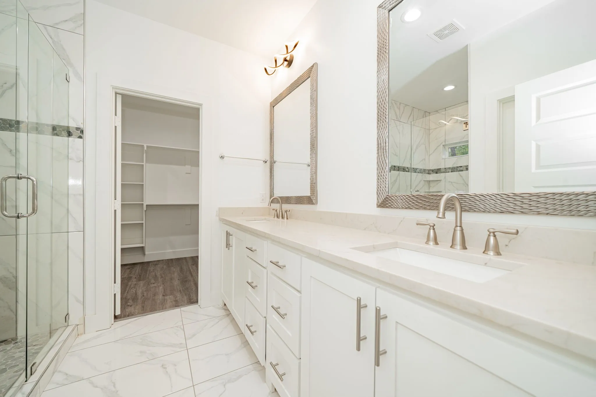 Dual sink vanity with stone-finish countertops, frameless glass shower enclosure, and white shaker cabinetry
