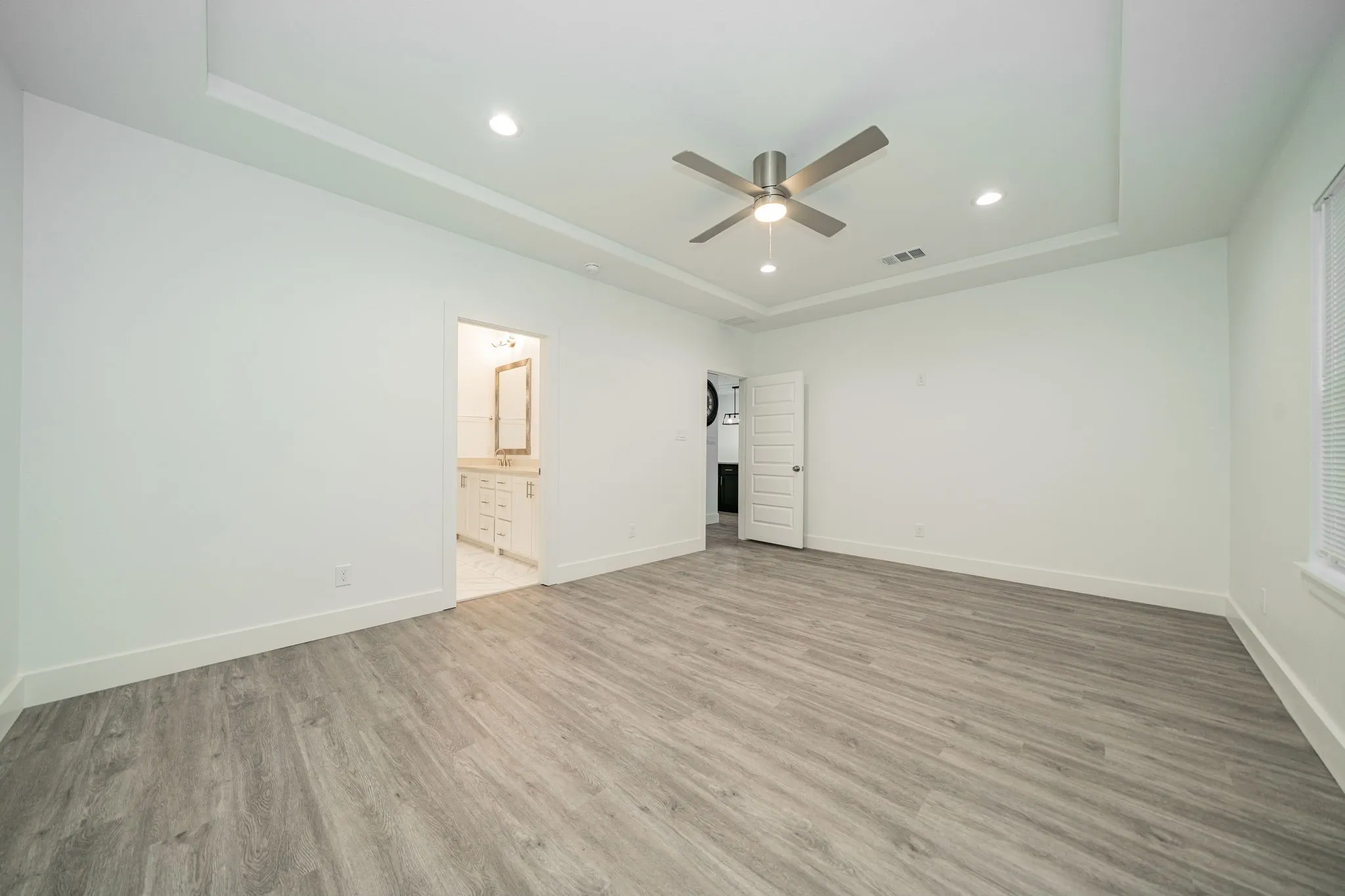 Wood-finish flooring throughout, tray ceiling, recessed lighting, ceiling fan, and white paneled interior doors