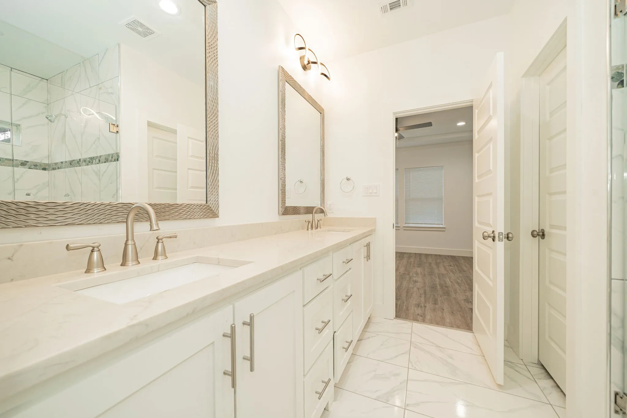 Dual vanity with integrated sinks, brushed nickel fixtures, custom framed mirrors, and marble-look tile flooring