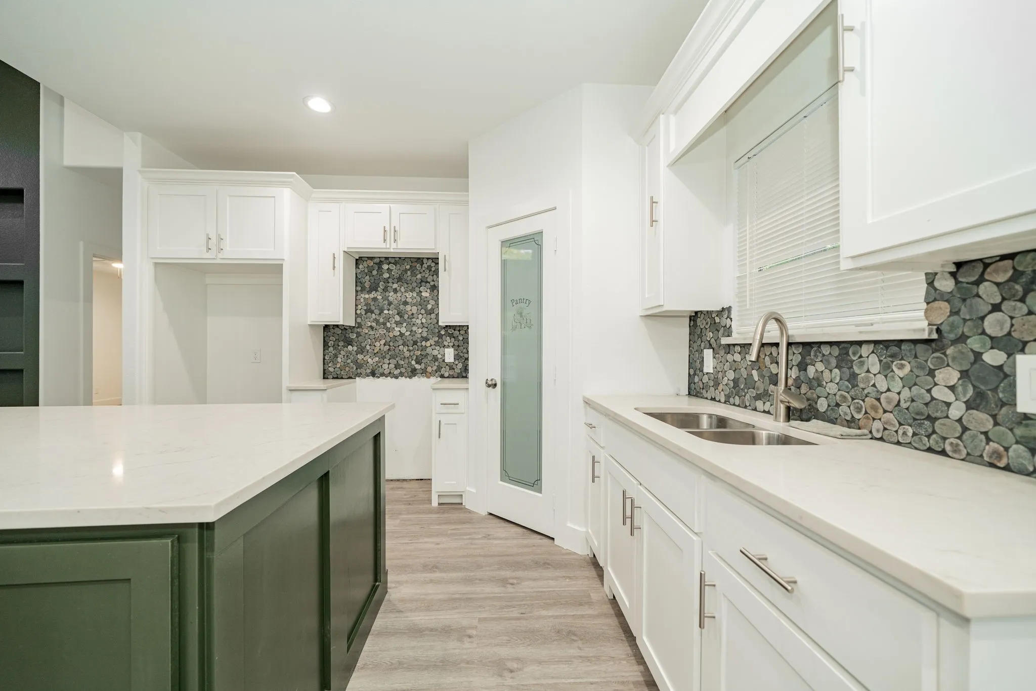 Kitchen featuring white cabinetry, light-toned countertops, a contrasting green island, pebble tile backsplash, and wood-finish flooring