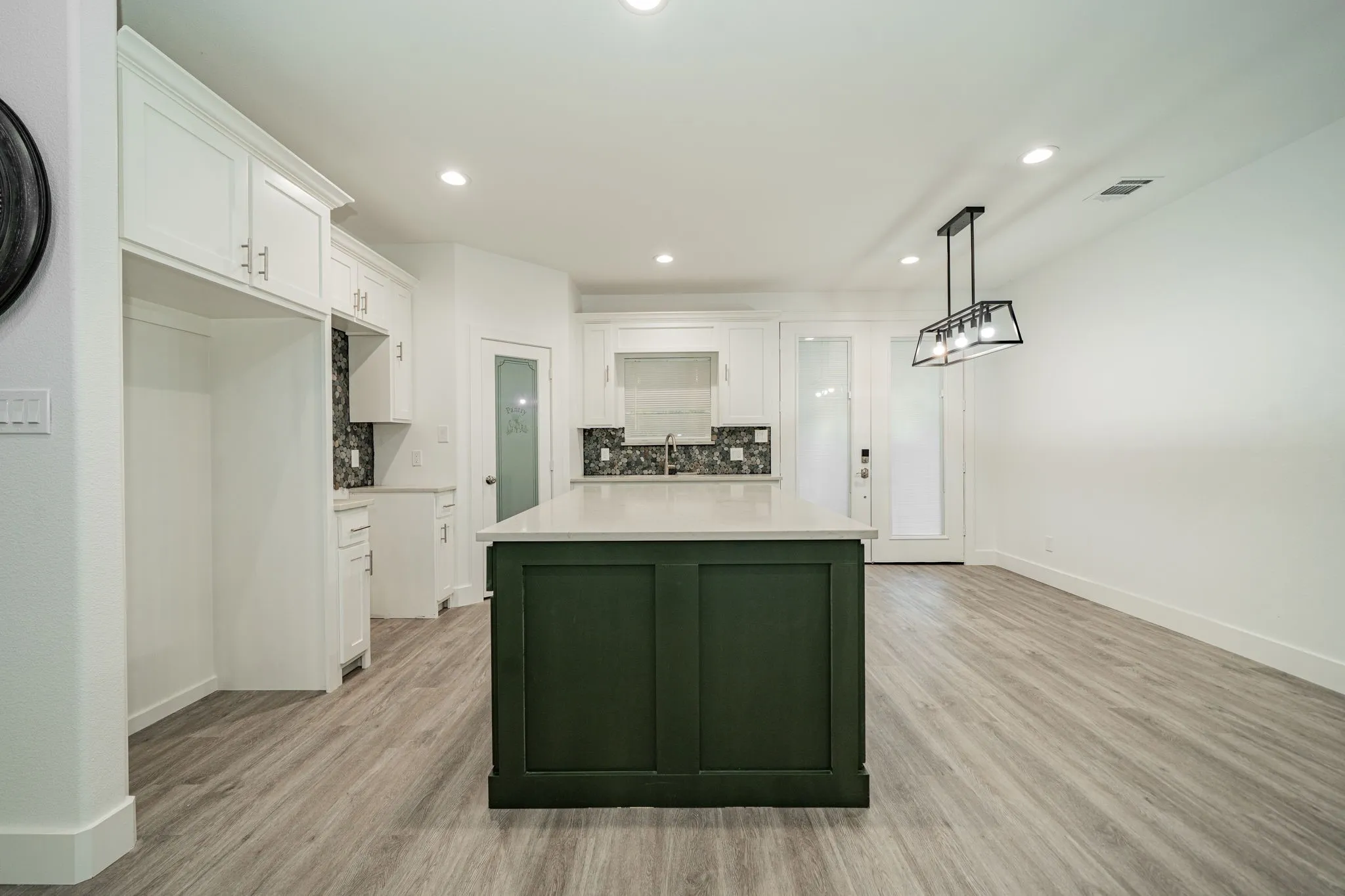 Open-concept kitchen featuring white shaker cabinetry, an island with dark green paneling and a light-colored countertop, and wood-finish flooring