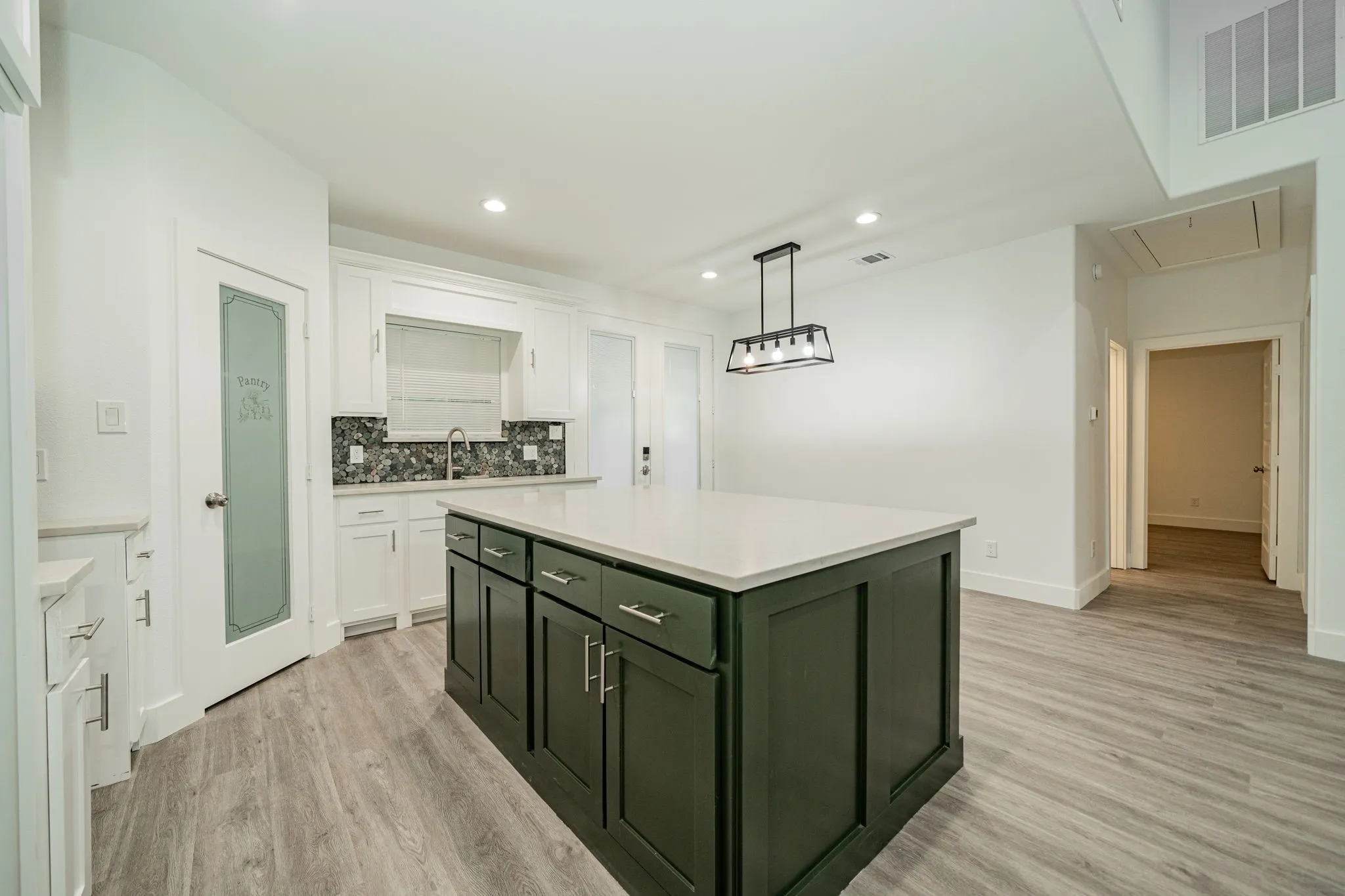 Kitchen featuring a dark green island, white cabinetry, light countertops, and a decorative backsplash