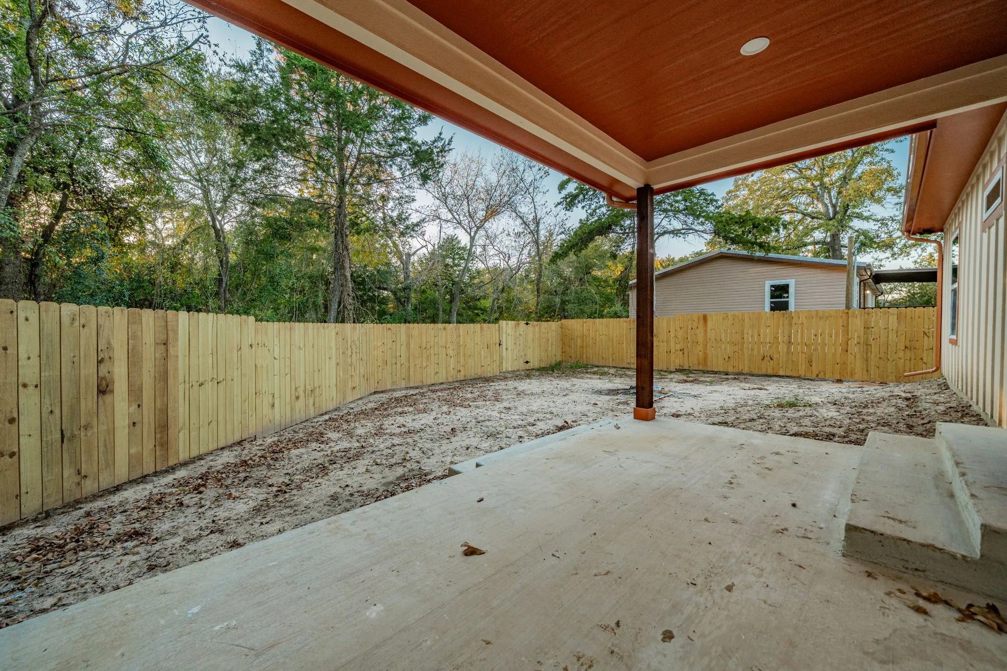 Covered concrete patio with recessed lighting, supported by a wood-finished column, and featuring a new wood privacy fence